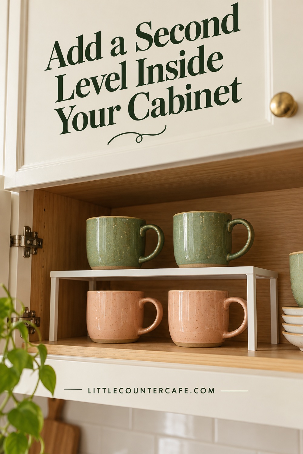 Two green mugs on a white shelf insert with two peach mugs beneath inside an oak cabinet.